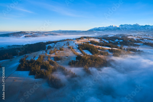 Drone view of Podhale highlands in Poland with winter frost, fog, and distant Tatra Mountains. Early morning light highlights the forested hills and valleys of this scenic mountain region.