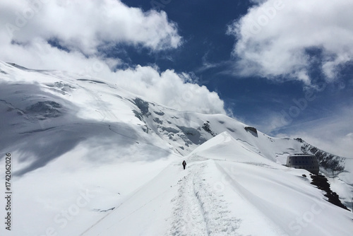 Snow-covered trail leading to Mont Blanc in the French Alps with a climber walking towards the summit.