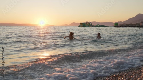 Сhild and a woman have fun swimming and splashing in the Adriatic sea during a beautiful sunset. A happy family enjoys their summer holiday at a resort in Podgora, Croatia. A joyful lifestyle moment.