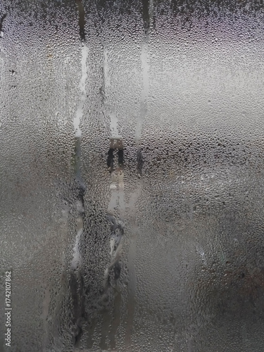 A close-up of a windowpane completely covered in tiny condensation droplets, with vertical streaks and a muted grey quality.