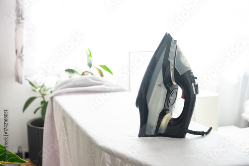 The iron is on the ironing board with a plain cloth in the room in close-up.