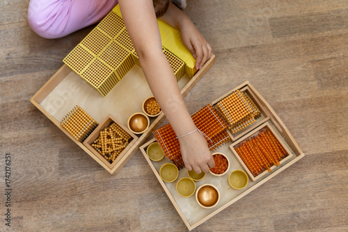 Child counts according to the Montessori method using golden material for mathematics, numbers, decimal number system. 