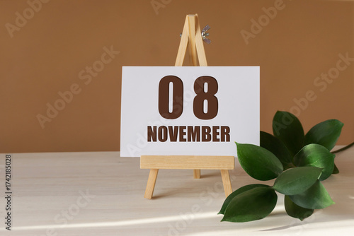 November 8th. Day 8 of month, Calendar date. Green branch, easel with the date and month on desktop. Close-up, brown background. Autumn month, day of year concept