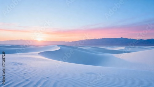 A serene desert landscape at sunrise, featuring undulating sand dunes under a soft pink and orange sky with distant mountains in the background.