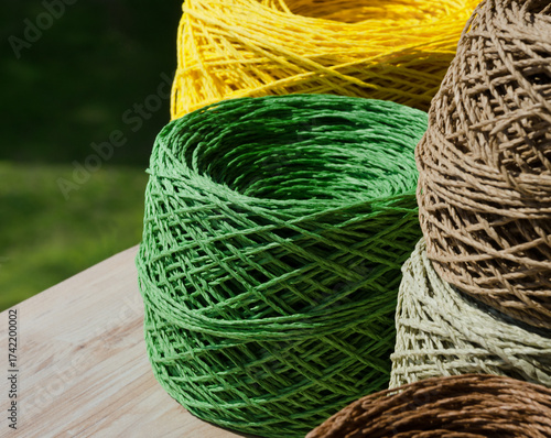 Natural raffia fibers are wound into spools against a background of green grass.