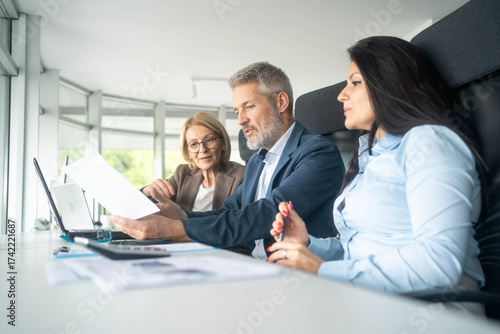 Three busy happy middle aged professional business man and two women executive leaders team using laptop working on computer at work desk having conversation on financial project at meeting in office.