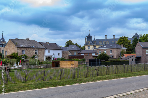 Landscape of gardens, farm orchards, country road and village brick houses with gray roof of castle in background against stormy sky, cloudy day on outskirts of Oud-Rekem, Limburg, Belgium