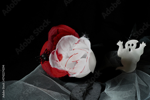Ghost figures beside artificial roses stained with blood over dark fabric. A spooky yet playful Halloween still life blending horror and fantasy in a mysterious atmosphere