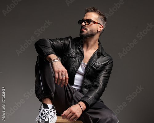 confident cool man with sunglasses looking to side and sitting with elbow on knee