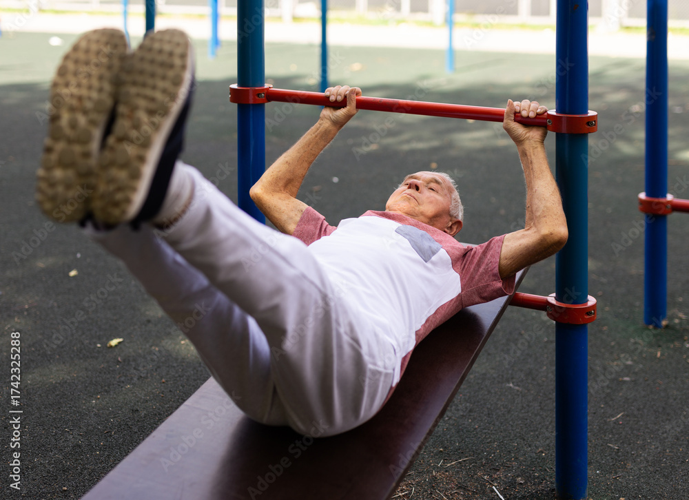 Fototapeta premium Old man doing leg raise exercise outdoors