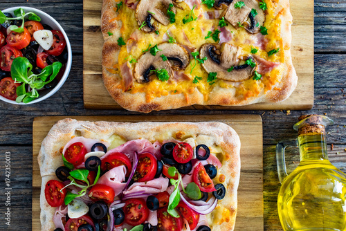 Two mini pinsa with varied toppings on wooden table. Top view