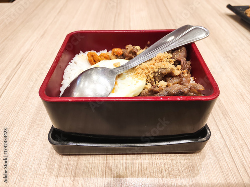 Top-table shot of a beef bento with egg, rice, and beef teriyaki. A traditional Japanese meat dish served on a wooden table.