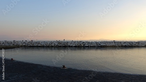 People in the distance enjoying the sunset light on the waterfront of Naples, Italy.