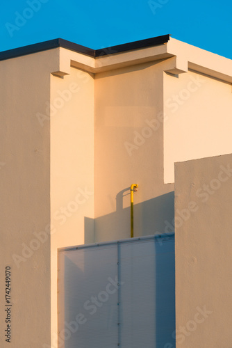 Minimalist architecture detail of modern building facade illuminated by warm sunset light, geometric shapes and clean lines against clear blue sky.