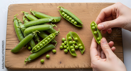 Close up of hands opening fresh green peas on a wooden board with more peas around it