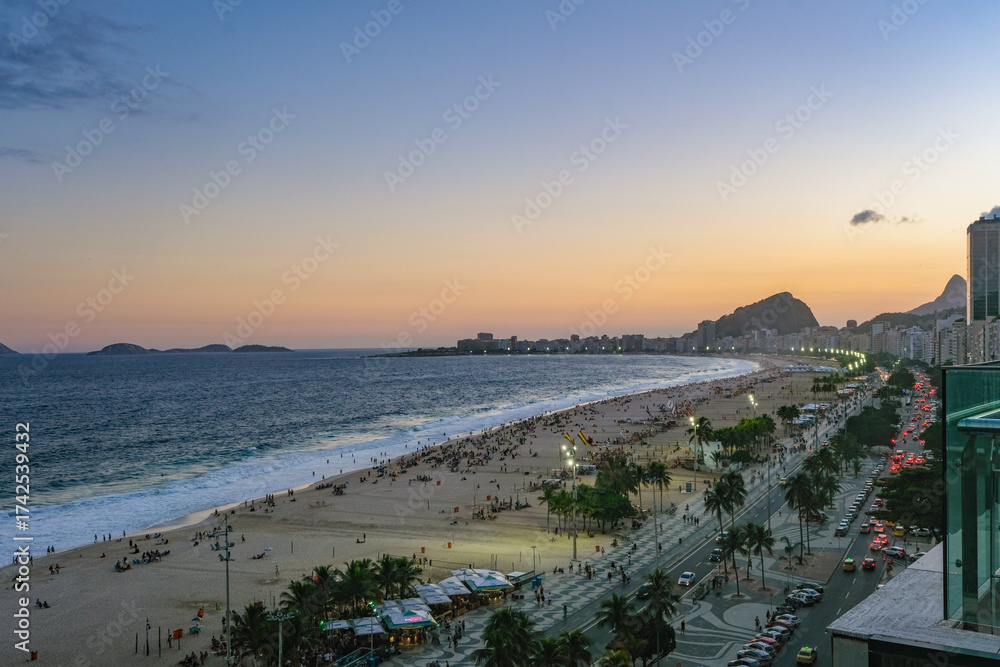 Fototapeta premium The breathtaking sunset over Copacabana Beach paints the sky with vibrant hues of orange and pink, reflecting on the Atlantic Ocean and illuminating Rio’s iconic skyline.