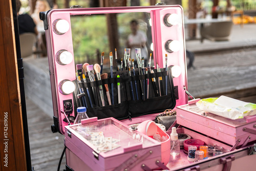 A pink makeup case with various brushes, lipsticks, and beauty products. The case is open, revealing organized tools for makeup application.