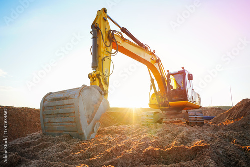 Excavator at construction site. Digger on construction site on sunset sky. Excavator moving soil for Sewage construction, Heavy Machinery dig trench. Earthmover on earthmoving. Sewer construction.