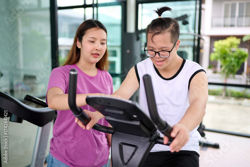 A young woman assisting a man with down syndrome exercising on fitness equipment