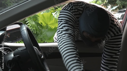 Masked thief reaching into car to steal valuable briefcase, view from inside the vehicle. Concept of crime, car theft, danger, security risk, and prevention awareness for property