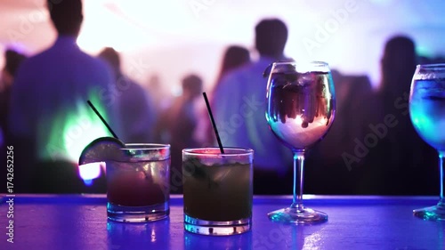 Alcoholic drinks on a bar at a wedding reception or night club with people partying and dancing in the background with haze, lasers, and lights.
