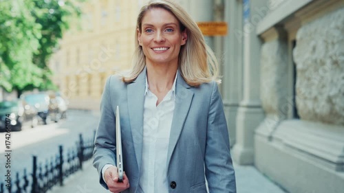 Confident Businesswoman Walking Outdoors Holding Laptop in City