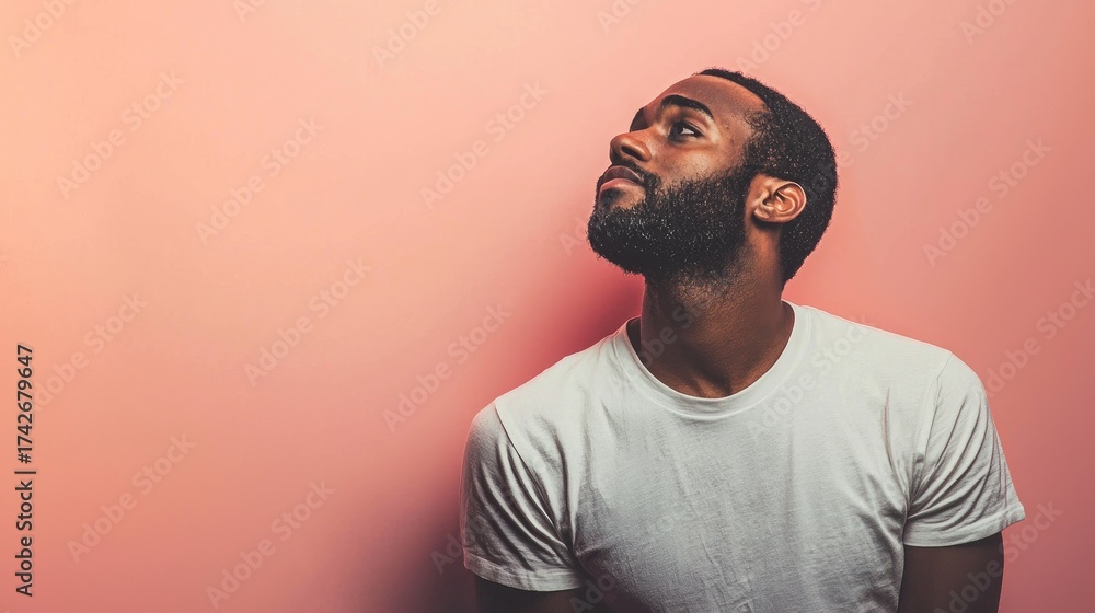 Obraz premium A man with a beard and mustache wearing a white t-shirt, standing against a pink background.