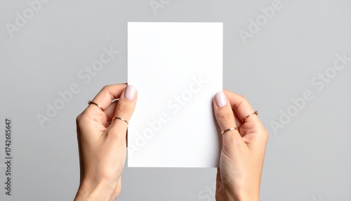 Female hands holding blank white card with gray background.