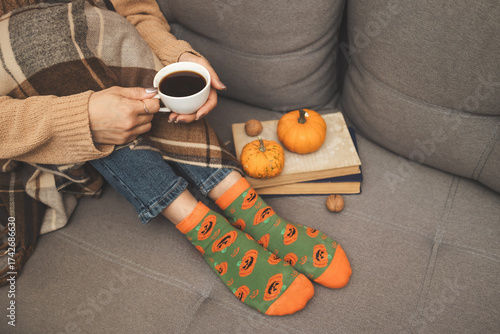 Cozy autumn scene, woman holding cup of coffee on couch with pumpkins, nuts, book and plaid blanket, warm seasonal atmosphere