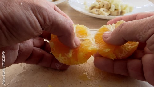 Human hands peel a tangerine orange and divide it into slices on a cutting board. Close-up.