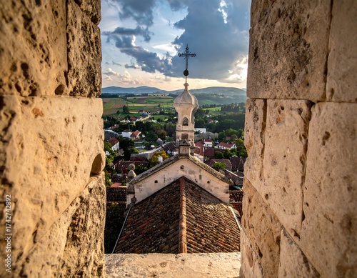 View of a church spire from a stone archway, over a town