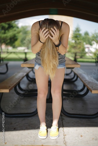 Woman with long blonde hair holding head in park 