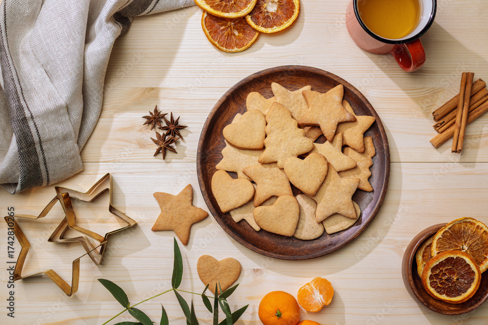 Fototapeta premium Overhead shot of a plate of cookies surrounded by oranges, star anise, dried orange slices, and a mug of tea.