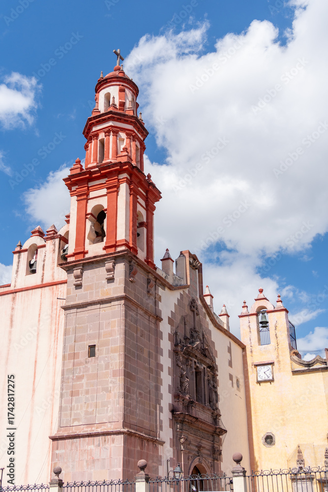 Fototapeta premium A large building with a red roof and a clock tower. The building is surrounded by a fence. Historic center of Queretaro, colonial architecture, decorations for the celebration of Mexico's Independence
