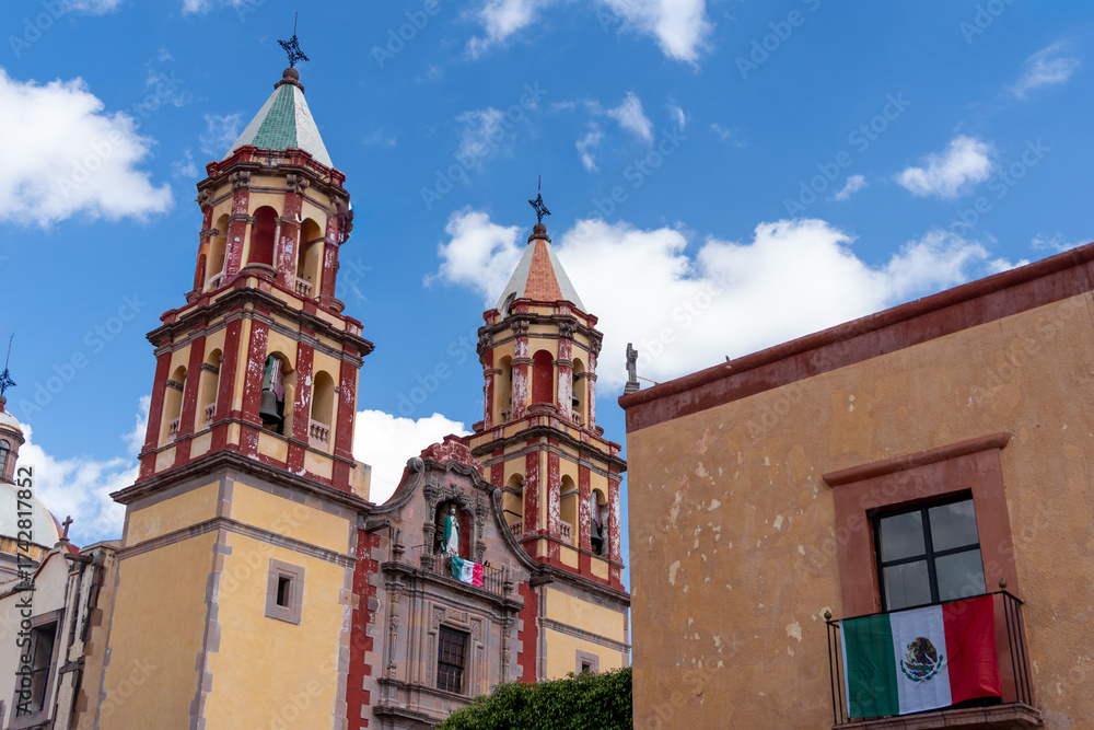 Obraz premium A historic building with two tall towers and a large window. The building is situated in a peaceful. Historic center of Queretaro, colonial architecture, decorations for the celebration of Mexico's In