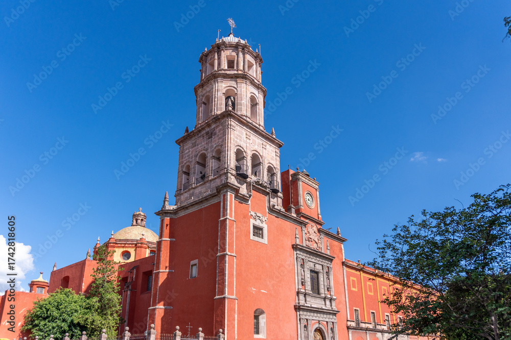 Obraz premium A beautiful red building with a tall tower and a blue sky in the background. Historic center of Queretaro, colonial architecture, decorations for the celebration of Mexico's Independence Day.