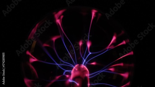 A stunning plasma globe radiates vibrant blue and pink electric arcs from its core, creating a mesmerizing and colorful display of static energy in the dark.