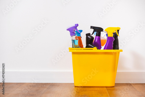 Bright multi-colored cleaning products, household chemicals bottles and sprays, rags, sponges in orange bucket for washing, wiping and dusting