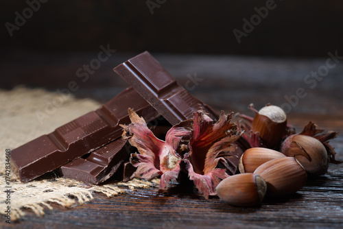 Broken dark chocolate with cocoa beans and hazelnuts on a wooden table