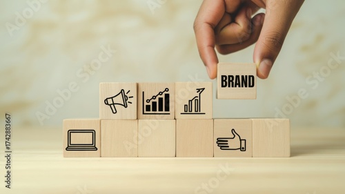 A hand places the BRAND block on top of other blocks with different marketing related icons. This creates a concept of brand awareness, brand building, marketing, and business growth