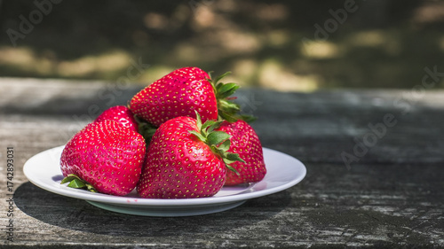 Fresh strawberries resting on a white plate atop a wooden table