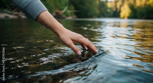 Hand dips into sunlit river, creating gentle ripples on the water