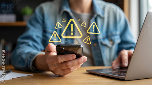 Urgent security alerts flashing on mobile phone screen as person works on laptop, cyber threat detected, warning signs, vulnerability found online