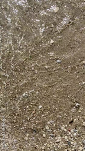 Close-up of sand, small stones, and sea waves