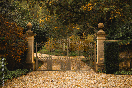 Fototapeta Wrought iron gates closing a gravel driveway leading to a secluded autumn estate
