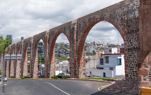 A stone arch bridge stretches across a street, connecting two sides of a city. Historic center of Querétaro, colonial architecture, decorations for the celebration of Mexico's Independence Day.