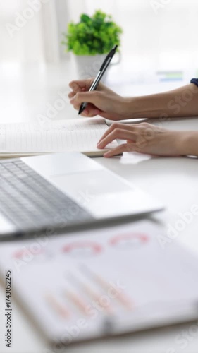 Professional businesswoman analyzing business charts while writing notes and pointing at laptop screen during strategic planning session.
