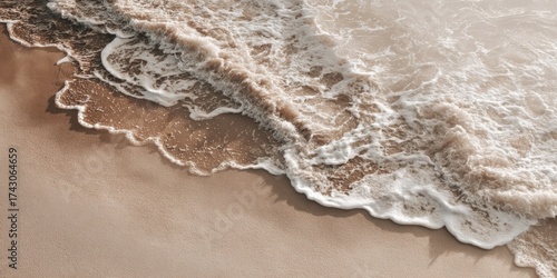 Overhead shot of waves crashing on sandy beach, with white foam and light brown hues