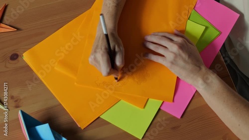 Top view of female hands drawing with pencil on colorful paper sheets