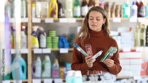 Young woman buyer chooses toothbrush in household chemicals store